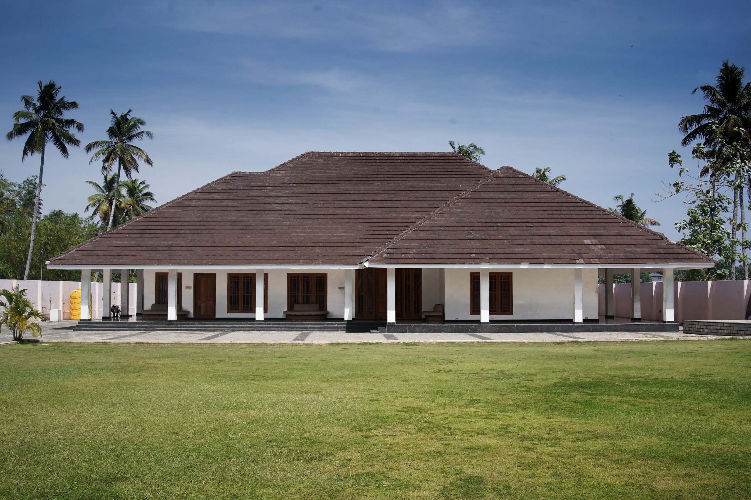 A traditional tropical bungalow surrounded by palm trees and lush green lawn.