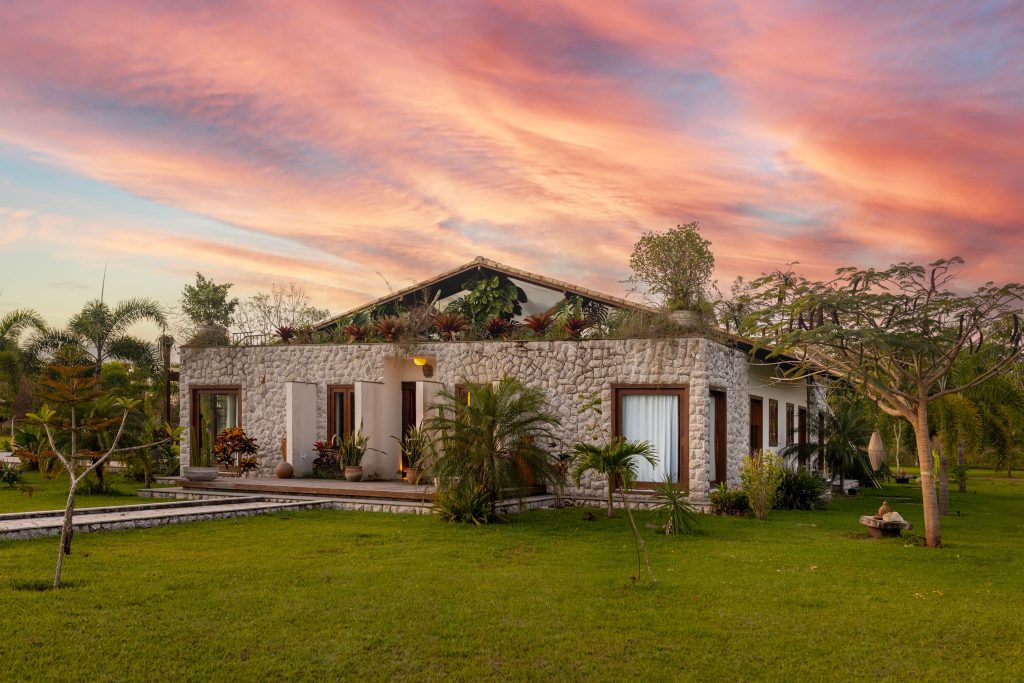 Beautiful stone house surrounded by lush garden under stunning sunset sky.